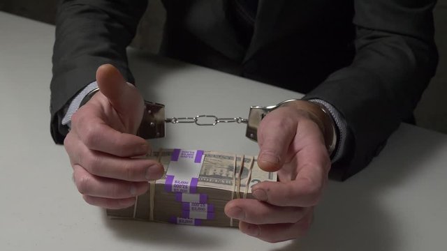 Businessmen in handcuffs offering cash money as bribery to get liberated.