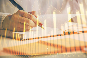 Double exposure of woman's hands making notes with forex graph hologram. Concept stock market analysis.