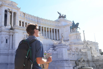 Tourist enjoying city sightseeing. Young man  looking into the map and smiling in a beautiful sunny day in Rome, Italy.