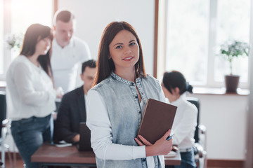 Stands in front of her colleagues. Group of people at business conference in modern classroom at daytime