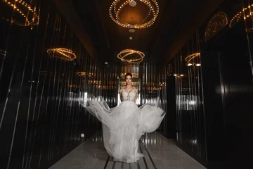 Foto op Plexiglas Mooie langbenige model meisje in een trouwjurk wandelen door de donkere hal in een luxe restaurant. Jonge vrouwenbruid in modieuze kleding. Concept huwelijksmode. © innarevyako