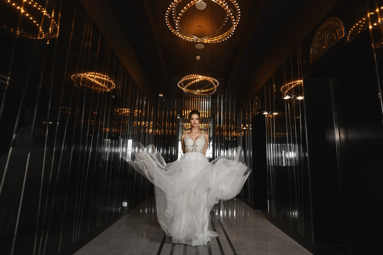 Beautiful leggy model girl in a wedding dress walking through the dark hall in a luxurious restaurant. Young woman bride in modish dress. Concept of wedding fashion.