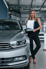 Fototapeta na wymiar Fashionable woman. Girl and modern car in the salon. At daytime indoors. Buying new vehicle