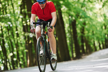 Naklejka premium Concentrated look. Cyclist on a bike is on the asphalt road in the forest at sunny day