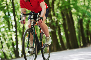 Cropped photo. Cyclist on a bike is on the asphalt road in the forest at sunny day