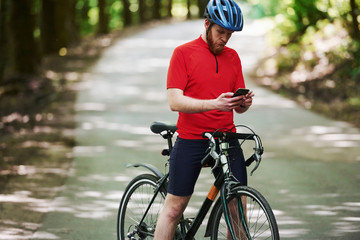 Naklejka premium Modern device. Cyclist on a bike is on the asphalt road in the forest at sunny day
