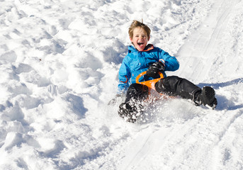 Fototapeta na wymiar Cute young boy laughing as he is sledging downhill in the snow