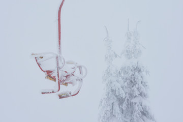 Frozen empty ski lift covered with snow on a foggy day.  Hard winter conditions, snowfall and fog.