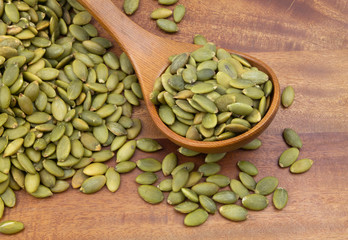 Pumpkin seeds and wooden spoon on wooden table