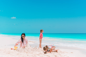Family making sand castle at tropical white beach. Mother and two girls playing with sand on tropical beach