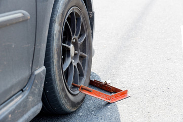 Locked wheel of a car parked in an improper place. Car wheels locked, traffic violation. Black car get locked up by the police. Illegal parking in the restricted area resulted in wheel