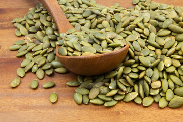 Green pumpkin seeds with wooden spoon on wooden table