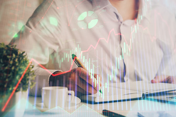 Double exposure of man's hands writing notes of stock market with forex chart.