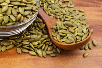 Green pumpkin seeds with wooden spoon and glass bowl