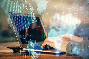 Double exposure of man's hands writing notes with laptop of stock market with forex graph background. Top View. Concept of research and trading.