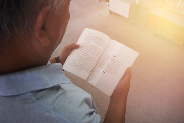 Old man with eye problems. He did not wear glasses. He holds the book in his hand and tries to read the book but can not read it because the text is not clear.