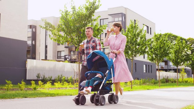 family, leisure and people concept - happy mother and father with little son in stroller walking along city street and drinking takeaway coffee