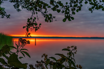 Sunrise - Sunset over a lake with a blurred background and green leaves - 296349187
