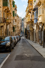 Fototapeta na wymiar Typical Valletta street architecture with traditional Maltese wooden enclosed balconies and rising road, at Valletta, Malta