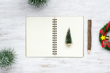 Top view of blank  notebook on grunge white wood  background with xmas toy decorations. Mockup Christmas background with notebook for wish list or to do list. Flat lay with copy space.
