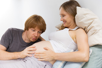 Cheerful future parents having fun at home. Surprise excited future dad staring at baby bump. Enjoying pregnancy concept