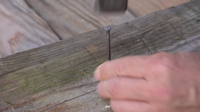 Man hammering nail into board hammer. Hands of an elderly man, the old hammer and nail. Close up. Detail of worker with a nail and a hammer