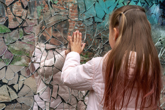 Young girl looks in a broken mirror and shows her hand on a mirror.