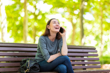 happy woman sitting on park bench talking with cellphone