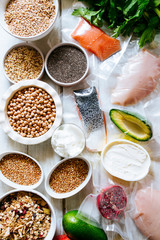 Variety of raw cereals  on  bowls, top view flat lay,lentils, bulgur and quinoa, hemp seed,sunflower seeds ,brown rice, rice, with some healthy food vacccum sealed salmon,avocado,chicken breast,concep