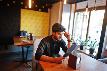 Confident young indian man in black shirt sitting at cafe and read menu.