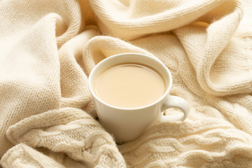 The white cup of hot coffee or tea with milk and the ivory color warm scarf