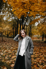 Autumn portrait of a young girl in an autumn park in a gray coat. Posing at a photo shoot in nature.