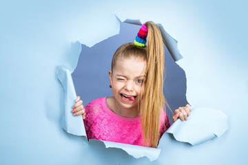 Portrait of lovely child smiling and winking looking on camera, pink shirt isolated over blue...