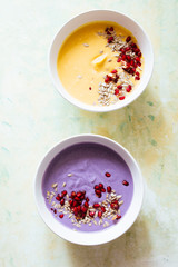 It's soup season, two bowls full of pumpkin and coconut soup one and the other violet potatoes soup, on a green and yellow  background,flat lay composition, healthy warm food for autumnal and winter s