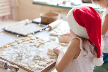 Kids cooking Christmas cookies in cozy home kitchen. Children prepare holiday food for family. Cute little girls bake homemade festive gingerbreads. Lifestyle moment. Santa helper.