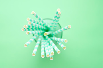 pile of paper striped white and green drinking straws for party in clear glass cup on green background