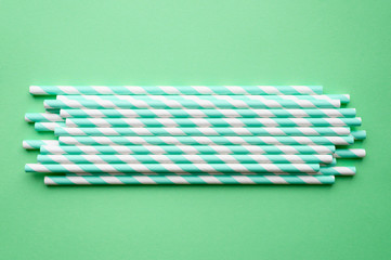 pile of paper striped white and green drinking straws for party on green background. space for text