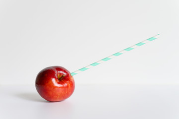 a ripe juicy bright red apple and in it a striped white and green paper drinking straw, located on a white background