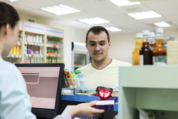 A female pharmacist standing at the cash register sells drugs to a man. The pharmacist counts the cost of the drug on the computer. A man buys medicine