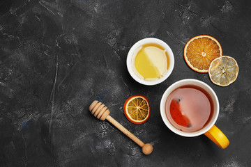 A cup of tea close-up on a dark background with dry citruses and honey. Top view.