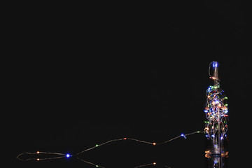 Glass bottle with beautiful glowing garland on dark background