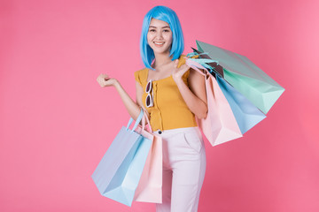 Portrait of a pretty excited asian girl with colorful shopping bags showing isolated over pink background .Asian shopaholic woman carrying shopping bags in colorful for summer sale concept .