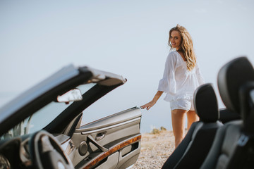 Pretty young woman by the white cabriolet car on the seaside