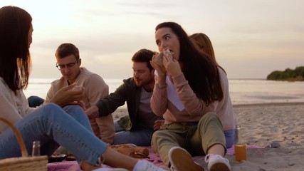 friendship, leisure and fast food concept - group of happy friends eating sandwiches or burgers at picnic on beach in summer - Powered by Adobe