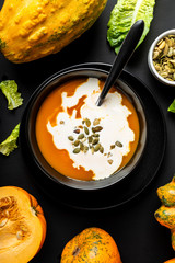 Pumpkin cream soup with milk and pumpkin seeds in a black bowl on the black background. Close-up.
