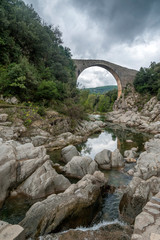 View of the old medieval bridge of Llierca, in the region of La Garrotxa, in Gerona (Spain), on a cloudy dramatic day. 