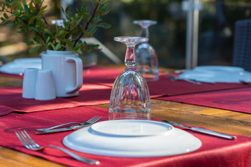 Elegant table setting with fork, knife, wine glass, white plate and red napkin in restaurant . Nice dining table set with arranged silverware and napkins for dinner