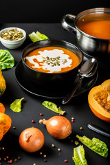 Pumpkin cream soup with milk and pumpkin seeds in a black bowl.
