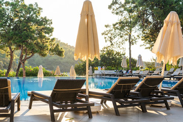 Empty sunbeds and closed parasols on morning, by the hotel pool. Swimming pool in luxury hotel...
