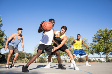 Young men playing basketball and dribbling ball on sports ground